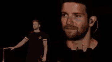 a man with a beard and ear buds is standing on a stage with his eyes closed .