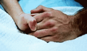 a person holding another person 's hand in a bed