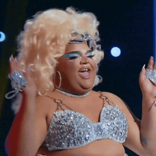 a drag queen is wearing a silver top and earrings
