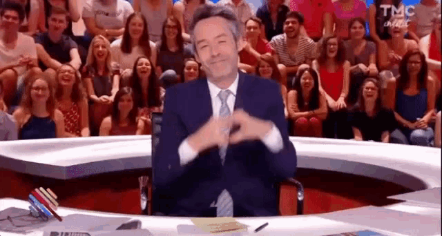 a man in a suit and tie is sitting at a desk in front of a crowd of people .