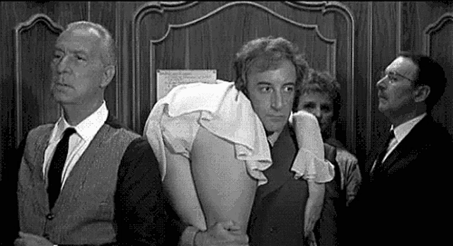 a man is carrying a woman on his shoulders in a black and white photo while other men look on .