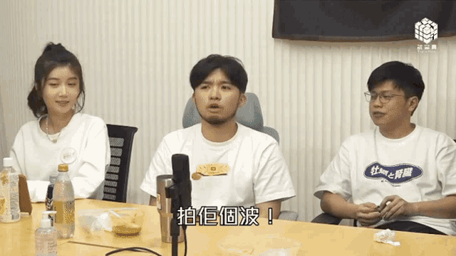 a group of people are sitting around a table and one of them is wearing a shirt with chinese writing on it