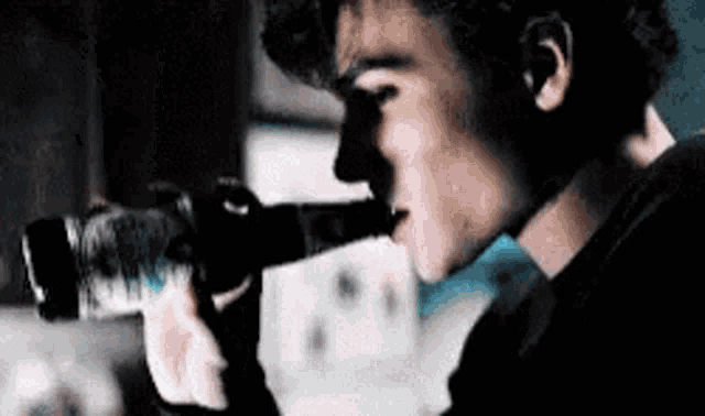 a man is drinking water from a bottle while looking through a telescope .