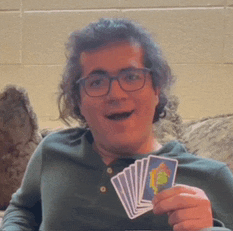 a man wearing glasses and a green shirt is holding a deck of cards .
