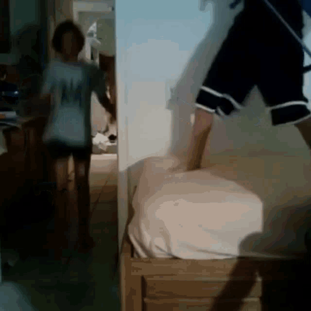 a person in a white shirt with the letter m on it is standing next to a bed .
