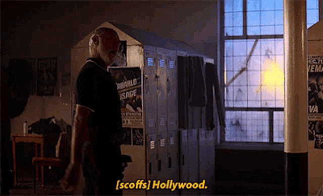 a man is standing in front of a row of lockers and says [ scoffs hollywood ]