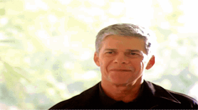 a man with gray hair and a black shirt looks at the camera