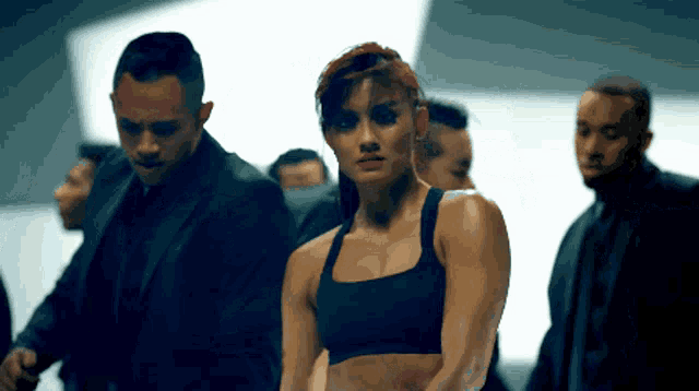 a woman in a black sports bra stands in front of a group of men