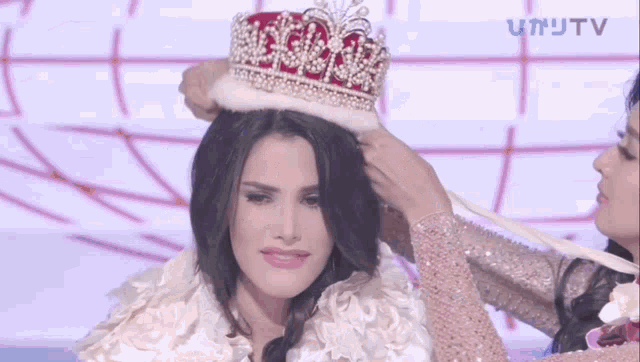 a woman wearing a crown is being adjusted by another woman in front of a tv screen