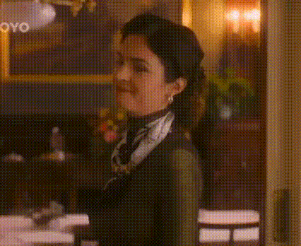 a woman wearing a scarf and earrings is standing in a room with candles in the background .