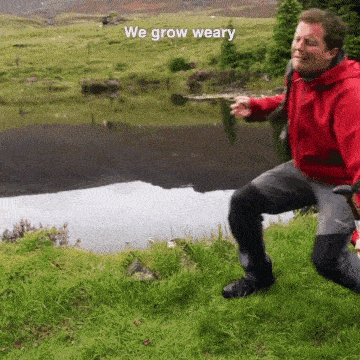a man in a red jacket is kneeling in the grass near a lake