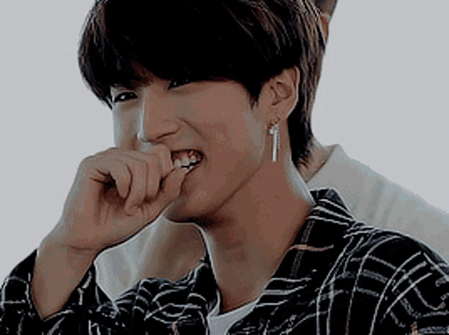 a young man wearing a plaid shirt and earrings bites his finger
