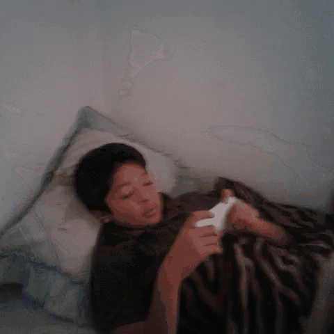 a young boy is laying on a bed playing a game