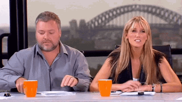 a man and a woman sit at a table with orange cups on it