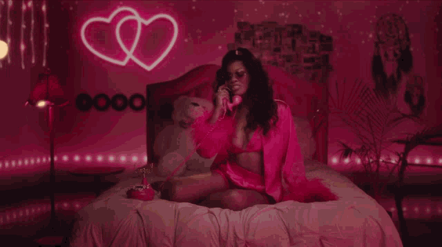 a woman is sitting on a bed talking on a pink telephone