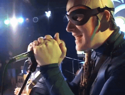 a man wearing a mask is singing into a microphone while holding a saxophone