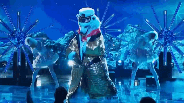 a polar bear is dancing on a stage with a group of dancers behind him .