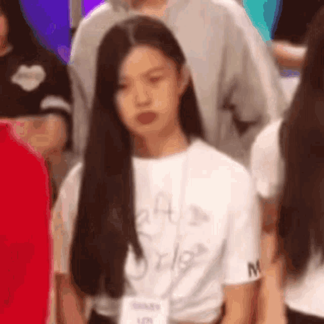 a woman with long black hair is standing in a crowd of people wearing a white shirt .