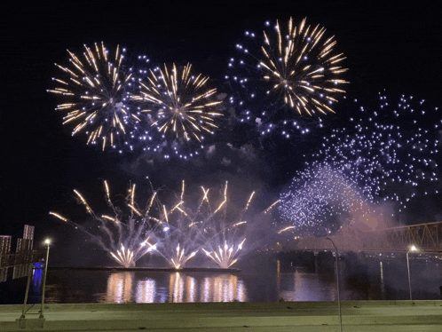 a fireworks display over a river with a bridge in the background