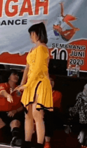 a woman in a yellow dress is dancing in front of a sign that says semarang