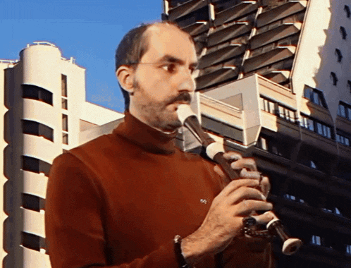 a man in a red sweater is playing a recorder in front of a building