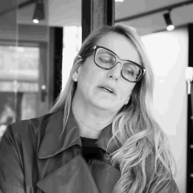 a woman wearing glasses stands in front of a window