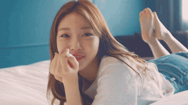 a woman is laying on her stomach on a bed and making a heart with her hands