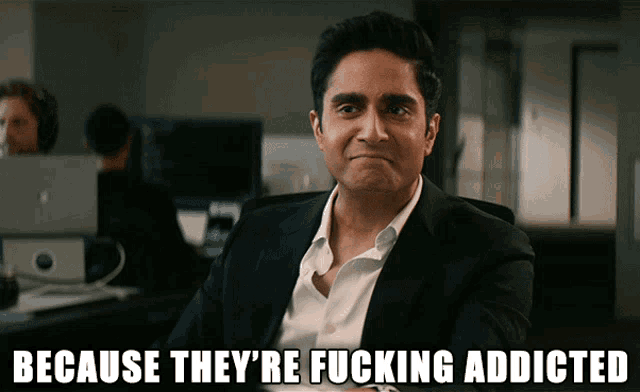 a man in a suit is sitting in front of a sign that says because they re fucking addicted