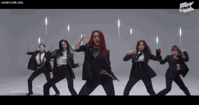 a group of women in suits are dancing in front of a sign that says thek
