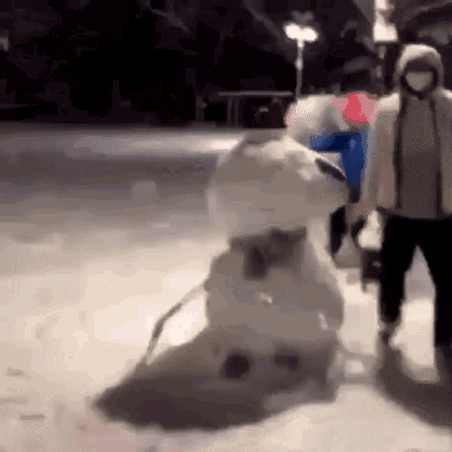a person is standing next to a snowman in the snow at night .