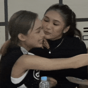 a woman kissing another woman 's cheek while holding a bottle of water
