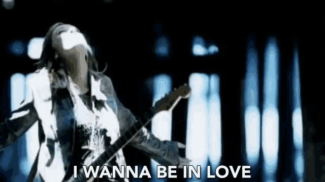 a woman is singing into a microphone while playing a guitar and says i wanna be in love .