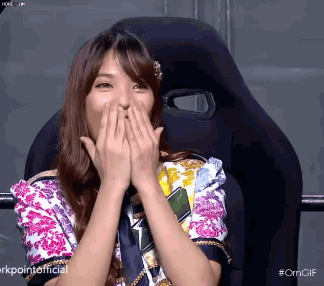 a woman covering her mouth with her hands while sitting in a chair ..