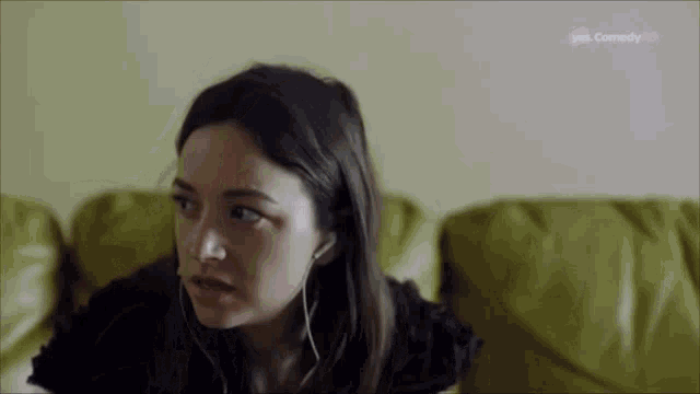 a woman is sitting on a couch wearing headphones and looking at the camera .