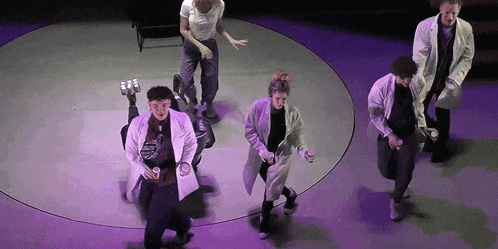 a group of people in lab coats are dancing in a circle on a stage