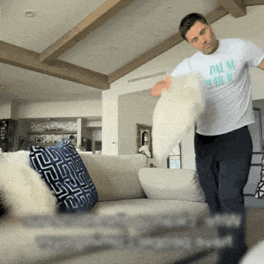 a man wearing a palm public t-shirt is standing in front of a couch