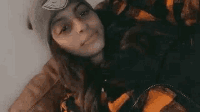 a young girl wearing a beanie and an orange jacket is smiling .