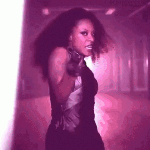 a woman in a black dress is pointing a gun in a pink room .