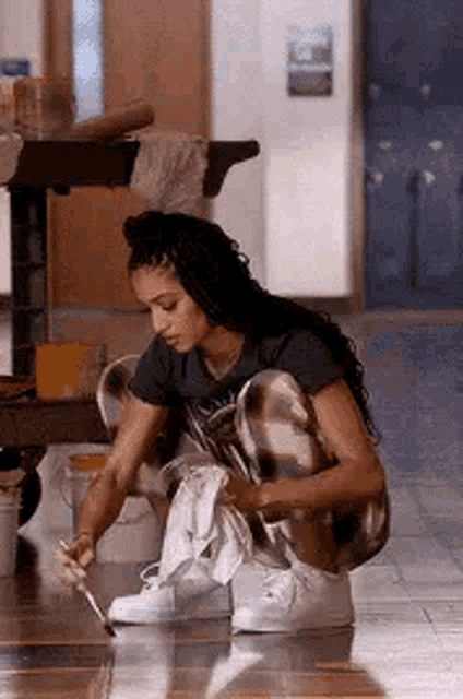 a woman is kneeling down on the floor painting a table .