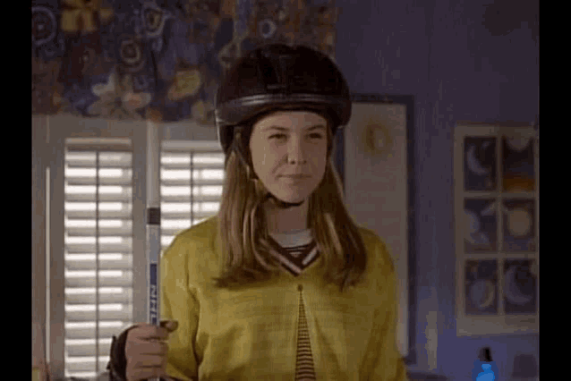a young girl wearing a helmet and holding a hockey stick in a room .