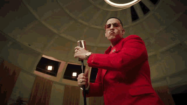 a man in a red suit and sunglasses is holding a microphone in a dome .