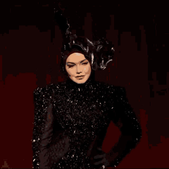 a woman in a black dress and hat is standing on a red stage .