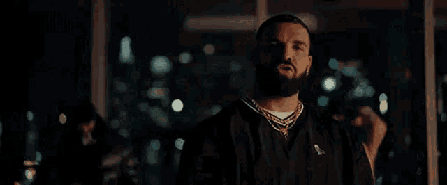 a man with a beard and a necklace is standing in front of a window in a room .