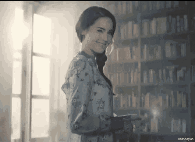 a woman in a blue dress is standing in front of a bookshelf and smiling