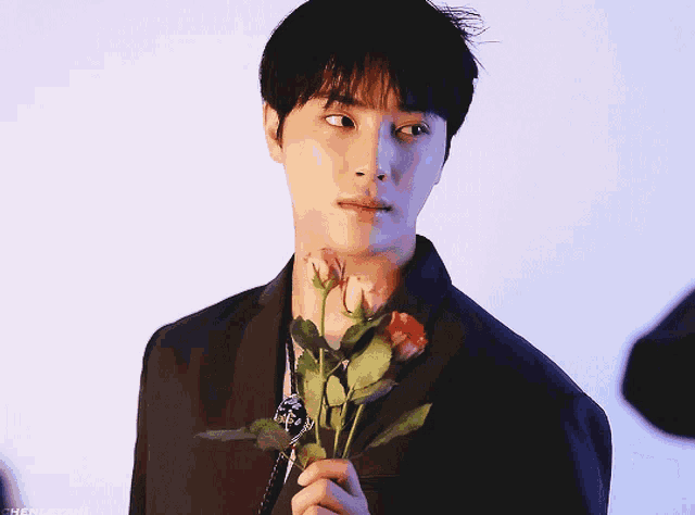 a man in a black suit holds a bouquet of roses