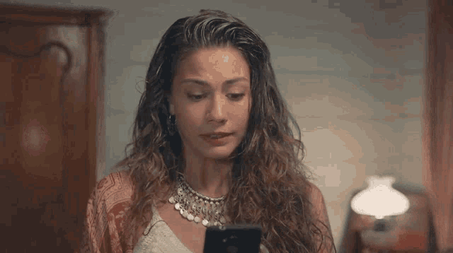 a woman with curly hair is looking at a cell phone