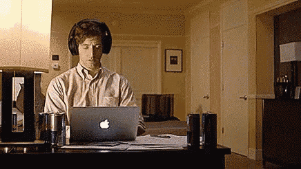 a man wearing headphones is sitting at a desk working on an apple laptop .