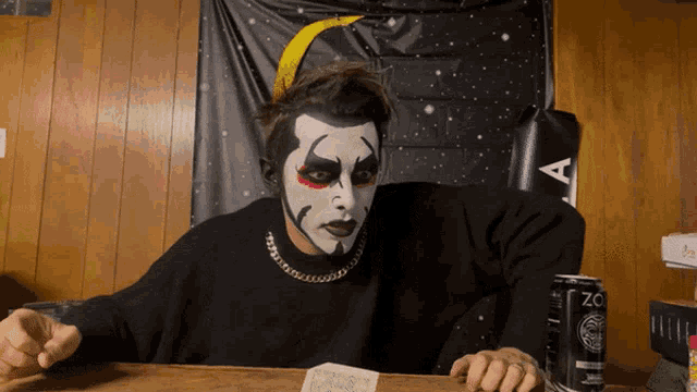 a man with face paint sitting at a table next to a can of zo