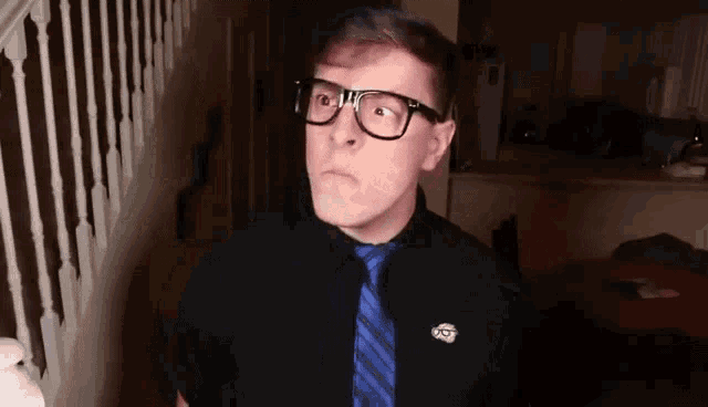 a man wearing glasses and a blue tie is standing in a hallway .
