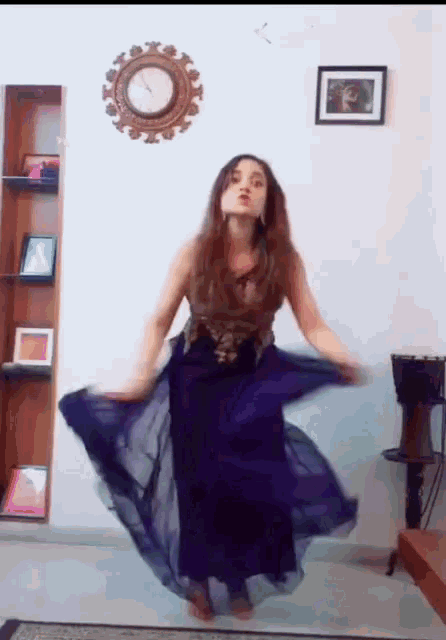 a woman in a long purple dress is dancing in front of a clock